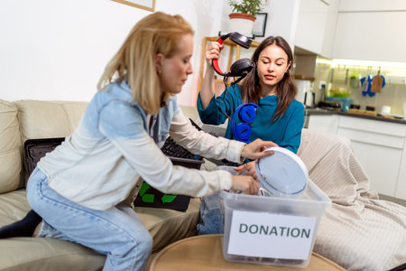 Two young girls are holding a donation box filled with old computer parts, getting ready to recycle them.の写真素材