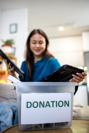 A young woman holds a donation box filled with old computer equipment, participating in an electronics recycling initiative.の写真素材