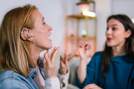 Two young girls are using sign language to talk to each other. One of them is wearing a hearing aid. They are smiling and enjoying the conversation.の写真素材