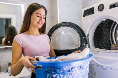 A young girl is taking fresh, clean laundry out of the dryer. She is smiling and doing her daily home chore.の写真素材
