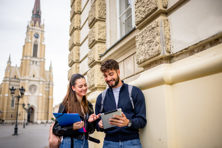 A teenage boy and girl walk side by side on a city street, holding literature books and sharing a tablet screen.の写真素材