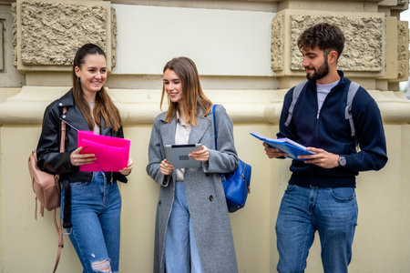 A group of three teenage students studying together. They are holding books and a tablet, discussing and sharing educational contentの写真素材