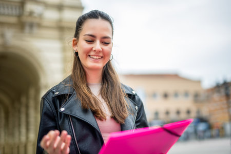 Portrait of happy female student who holds folder while her classmates are in the background.の写真素材