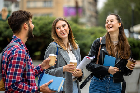 Three university students studying together outside on a sunny day. One student brought coffee to go, adding a casual  touch to the study session.の写真素材