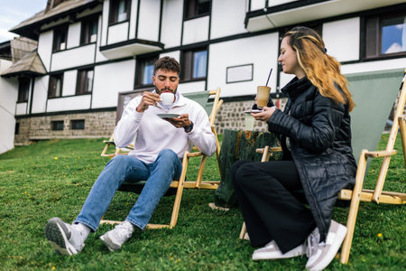 A young man and woman relax on lounge chairs during a weekend getaway at a mountain resort. Surrounded by nature and fresh air, they savor hot coffee and refreshing juice.の写真素材