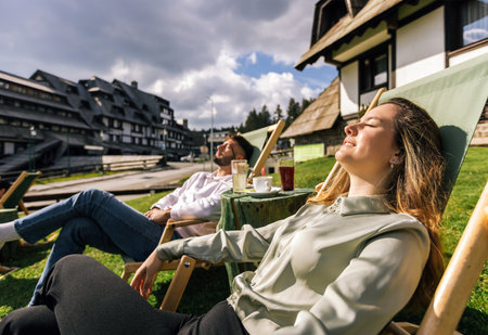 A young man and woman relax on lounge chairs at a mountain resort during a sunny weekend escape.の写真素材