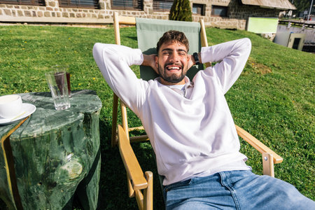 A young man relaxes on a lounge chair at a mountain resort during a sunny weekend escape.の写真素材