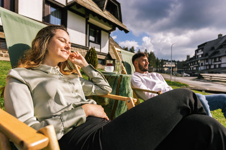 A young man and woman relax on lounge chairs at a mountain resort during a sunny weekend escape.の写真素材