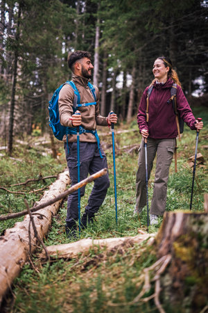 A young man and woman are captured hiking through a lush mountain forest, fully equipped with...