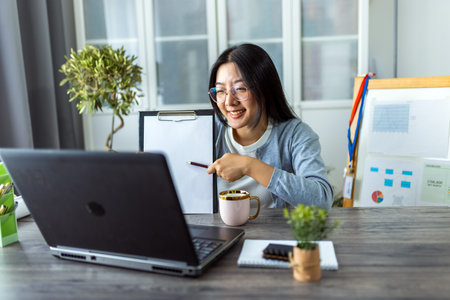 A young Thai woman is working from home and participating in a business video call.の写真素材