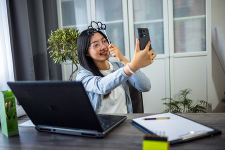 A young Thai woman is having fun while taking a selfie wearing a playful fake crown.の写真素材