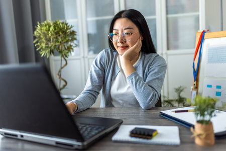 A young Thai woman is working from home, focused on her computer in a cozy home office setting.の写真素材