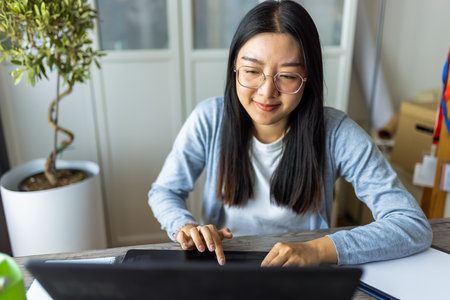 Thai woman sits at a desk in a comfortable home environment, focused on her computer as she works remotely.の写真素材