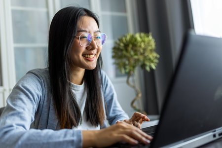 Thai woman sits at a desk in a comfortable home environment, focused on her computer as she works remotely.の写真素材