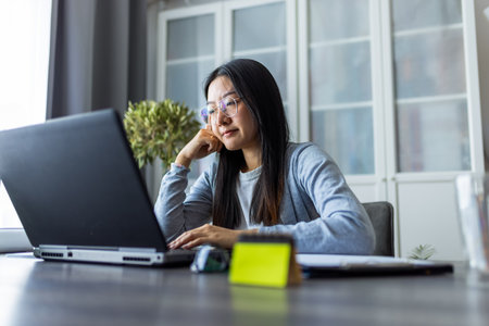 Thai woman sits at a desk in a comfortable home environment, focused on her computer as she works remotely.の写真素材