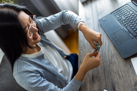 A young Thai woman works from home on her computer while taking medicine, showing a moment of self-care during her busy remote workday.の写真素材