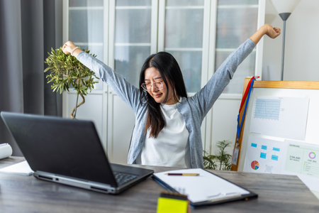A young Thai woman working from home on her computer looks exhausted and stretches her arms and head to relieve tension.の写真素材