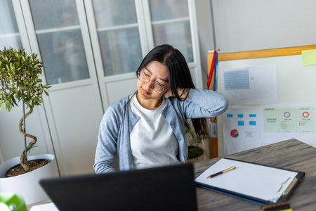 A young Thai woman working from home on her computer looks exhausted and stretches her arms and head to relieve tension.の写真素材