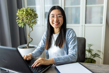 Thai woman sits at a desk in a comfortable home environment, focused on her computer as she works remotely.の写真素材