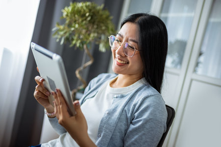 A young Thai woman is working from home, focused on her tablet device.の写真素材