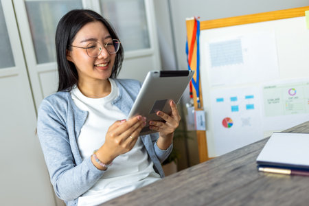 A young Thai woman is working from home, focused on her tablet device.の写真素材
