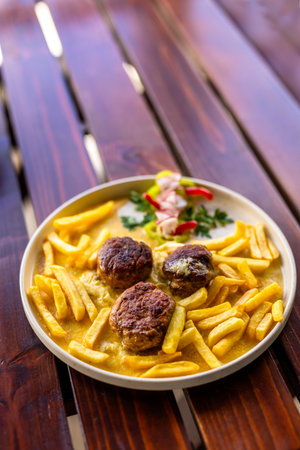 Juicy meatballs served with golden French fries on a white plate. A hearty, classic comfort meal captured in natural light.の写真素材