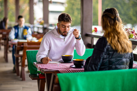 Young couple enjoying lunch together at a mountain resort restaurant terrace during a sunny autumn or spring day.の写真素材