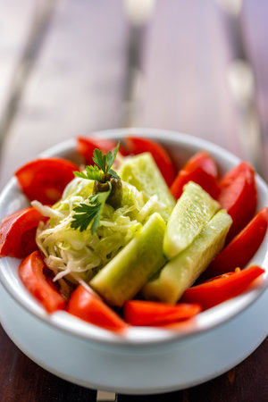 Fresh cucumber and tomato salad served in a bowl on a wooden table.の写真素材