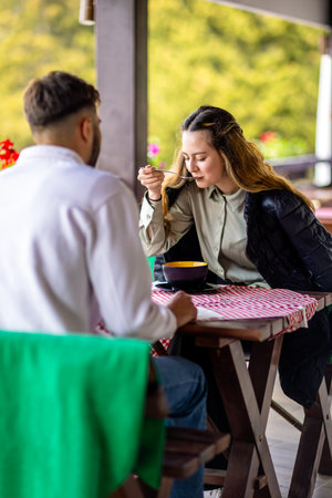 Young couple enjoying lunch together at a mountain resort restaurant terrace during a sunny autumn or spring day.の写真素材