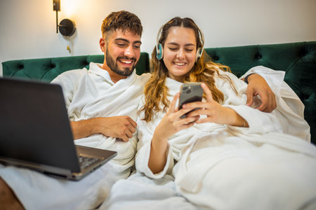 A loving couple relaxes in bed, closely looking at a smartphone together.の写真素材