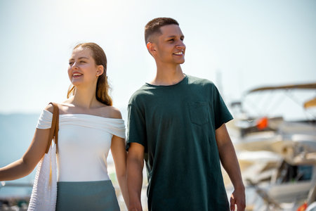A young couple walks hand in hand around a marina deck, surrounded by luxurious yachts.の写真素材