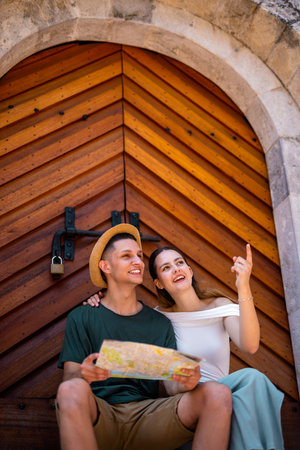 A young couple sits together by the ancient gate of a historic old city during their summer holiday, examining a map as they plan their next adventure.の写真素材