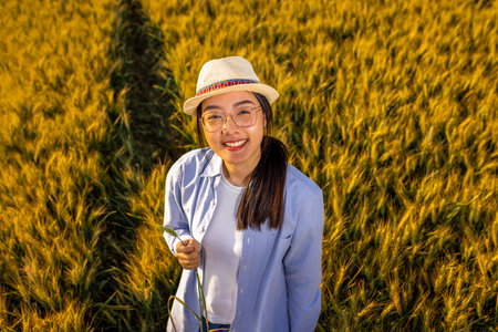 A Thai female farmer stands in a golden wheat field holding wheat stalks and smilingの写真素材