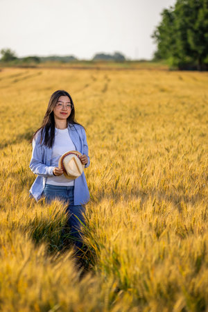 A Thai woman farmer stands confidently in a golden wheat field.の写真素材