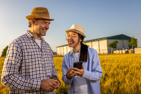 A Thai female farmer and a senior male farmer stand in a golden wheat field looking at a smartphone together.の写真素材