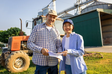 A young Thai woman and an older male farmer stand together on a sheep farm, engaged in a discussion about upcoming tasks.の写真素材