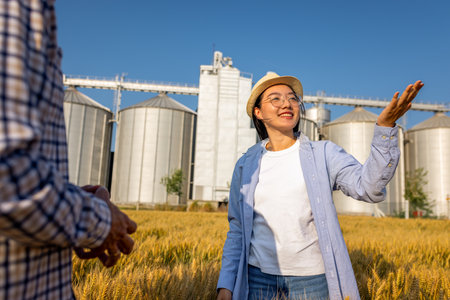 Two workers stand in a wheat-covered area in front of large silos, actively discussing upcoming tasks.の写真素材