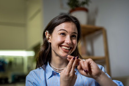 A joyful young woman sits in her living room wearing a hearing device, communicating confidently through sign language.の写真素材