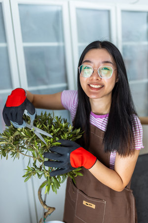 A young Thai girl is carefully cutting the leaves of her houseplant, maintaining its health and appearance.の写真素材