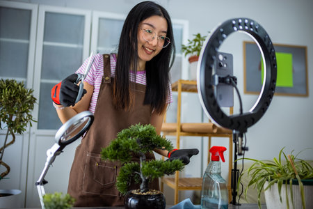 A young Thai influencer carefully trims her bonsai tree while recording a video with a ring light.の写真素材