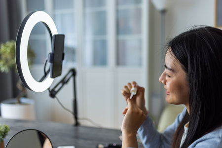 A young Thai beauty influencer films a nail painting tutorial using a ring light at home.の写真素材