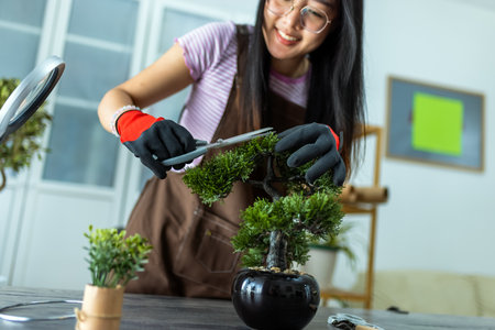 A young Thai girl carefully trims her bonsai tree, practicing patience and precision.の写真素材