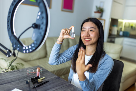 A young Thai influencer proudly shows off her freshly painted nails while filming a beauty video with a ring light.の写真素材