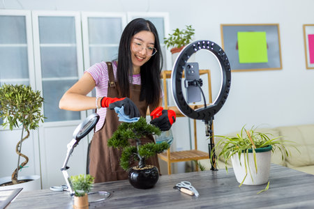 A young Thai influencer films a lifestyle video with a ring light while gently cleaning her houseplant leaves using water and a cloth.の写真素材