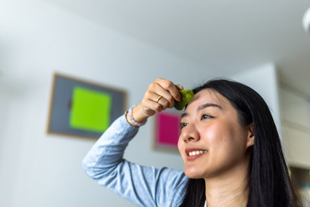 A young Thai influencer demonstrates her gua sha facial massage routine while filming a skincare video with a ring light.の写真素材