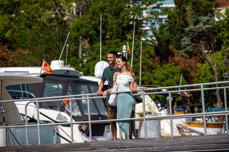 A young couple stands on a marina bridge with the boyfriend hugging his girlfriend from behind, both gazing peacefully at the sea.の写真素材