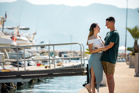 A young couple on summer vacation stands by the marina deck, holding each other closely and gazing into each otherâs eyes.の写真素材