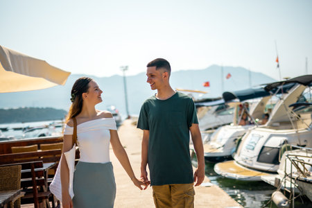 A young couple walks hand in hand along the sunny promenade, looking lovingly at each other.の写真素材