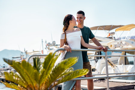 A young couple stands on a marina bridge with the boyfriend hugging his girlfriend.の写真素材