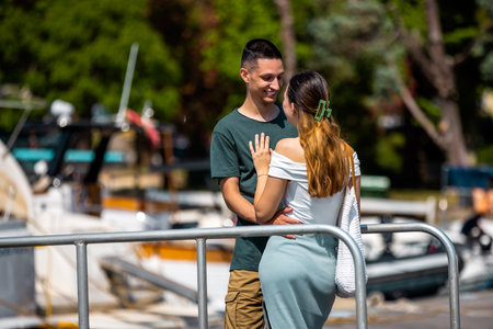 A young couple stands on a marina bridge with the boyfriend hugging his girlfriend.の写真素材